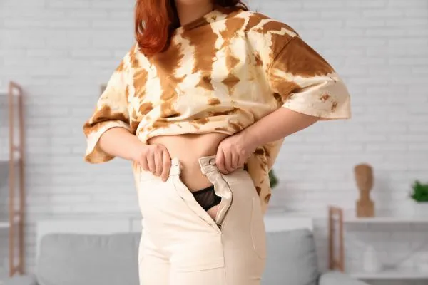 Image of woman trying to do her trousers up after pregnancy weight gain London