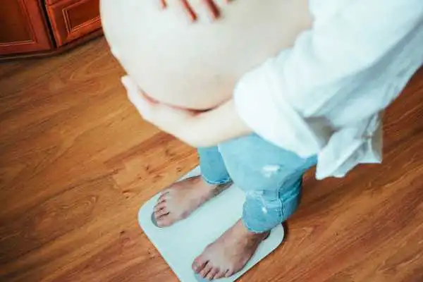 Image of woman weighing herself and experiencing weight gain through pregnancy London